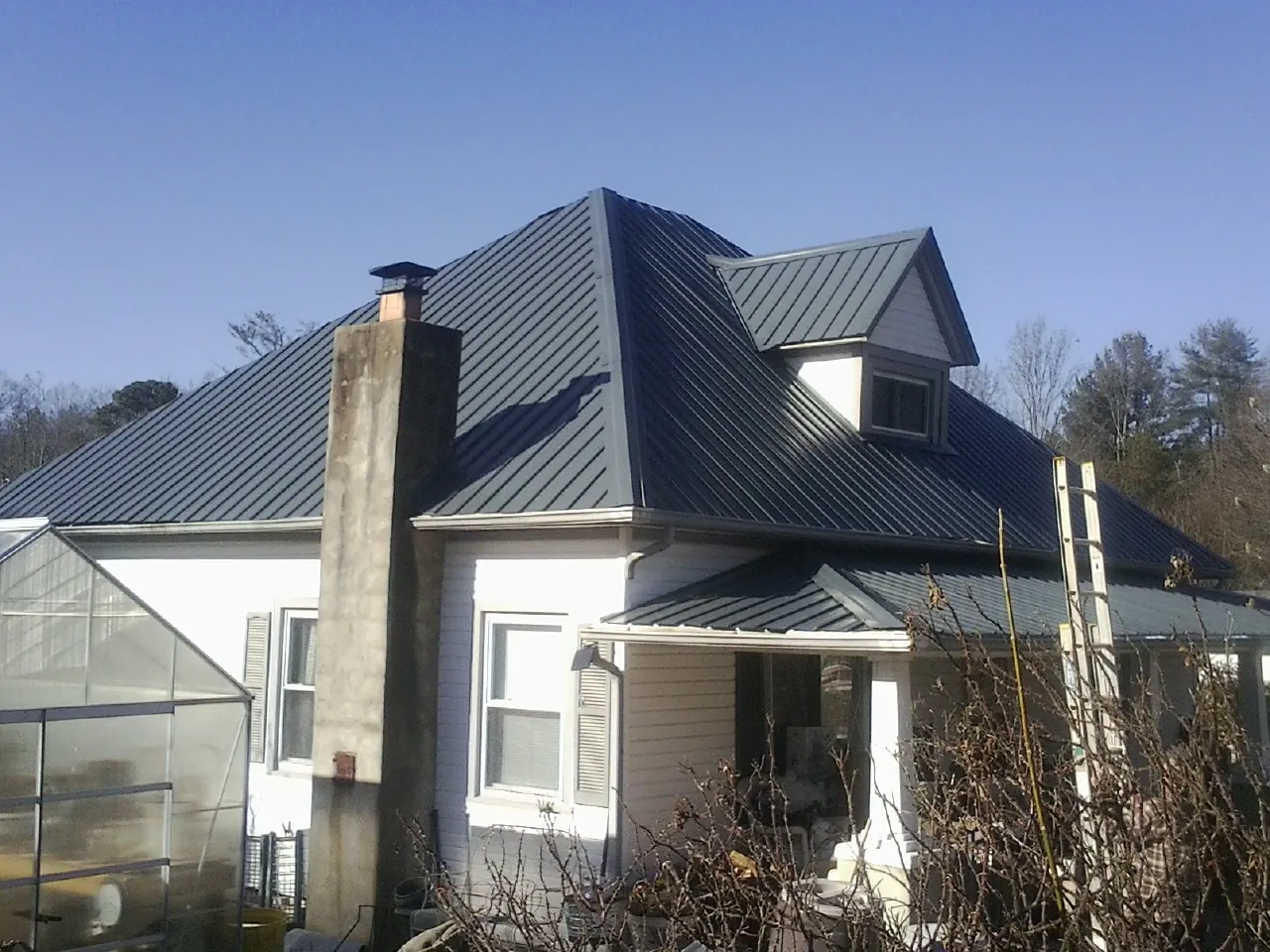 Dark blue standing seam metal roof on a white farmhouse with dormer — Slate & Tile Roof Repair by Roofing Brothers in Lucama