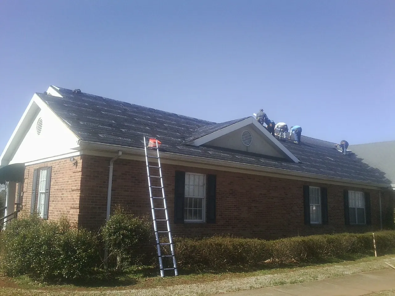 Crew tearing shingles off a brick ranch roof with a ladder set — Metal Roof Repair work by our crew in Lucama