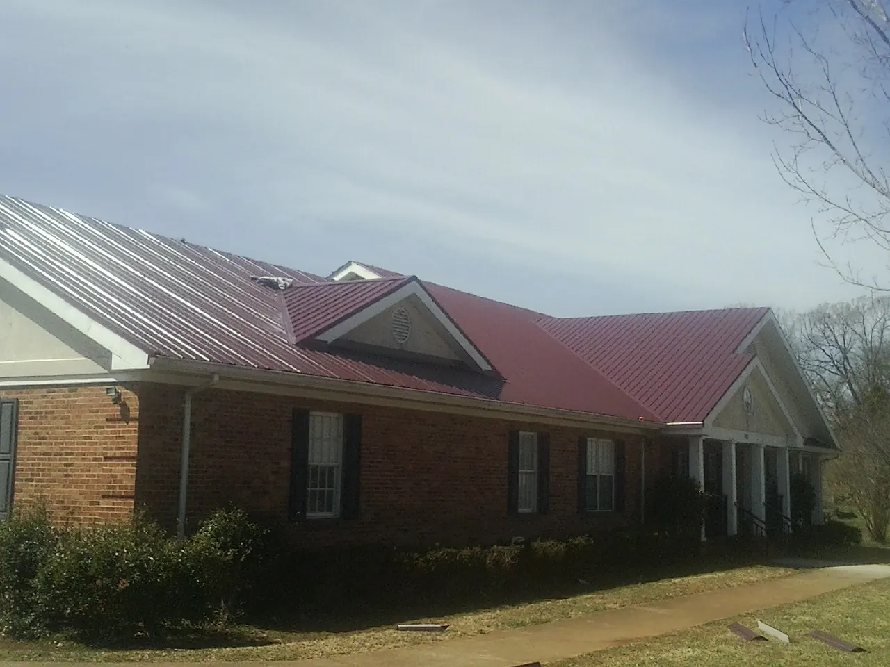 Red metal roof with gabled entries on a long brick building, from a Hail Damage Roof Repair job in Lucama
