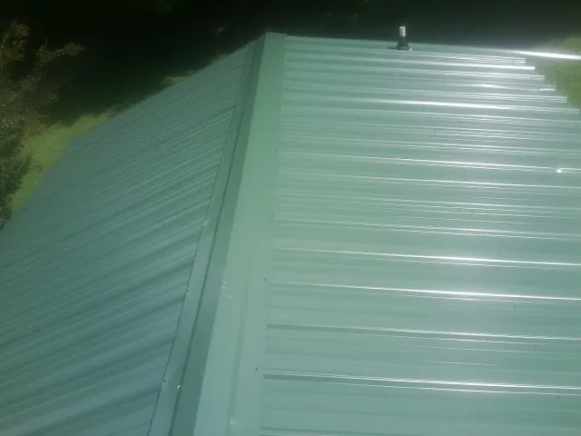 New green metal panels meeting at the ridge of a roof — Flat Roof Repair work by our crew in Lucama