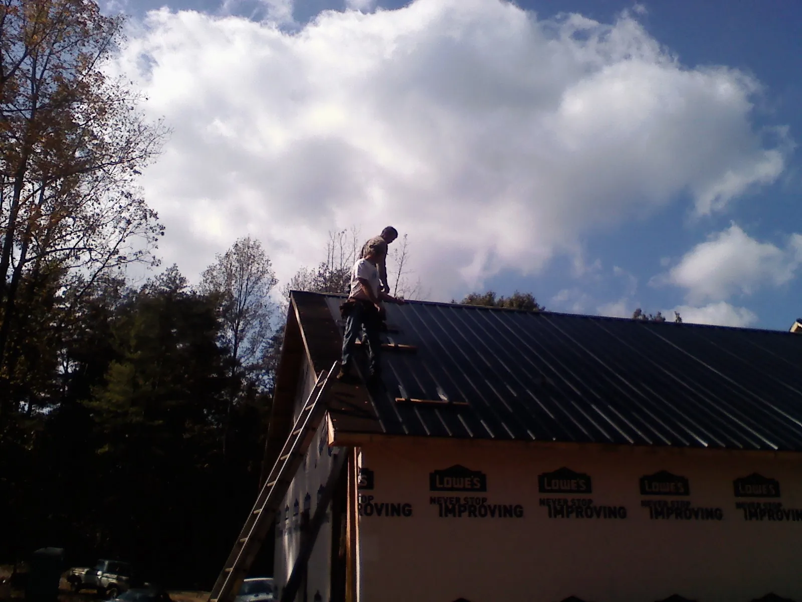Roofer fastening dark metal panels high against a cloudy sky, from a Roof Inspection job in Lucama