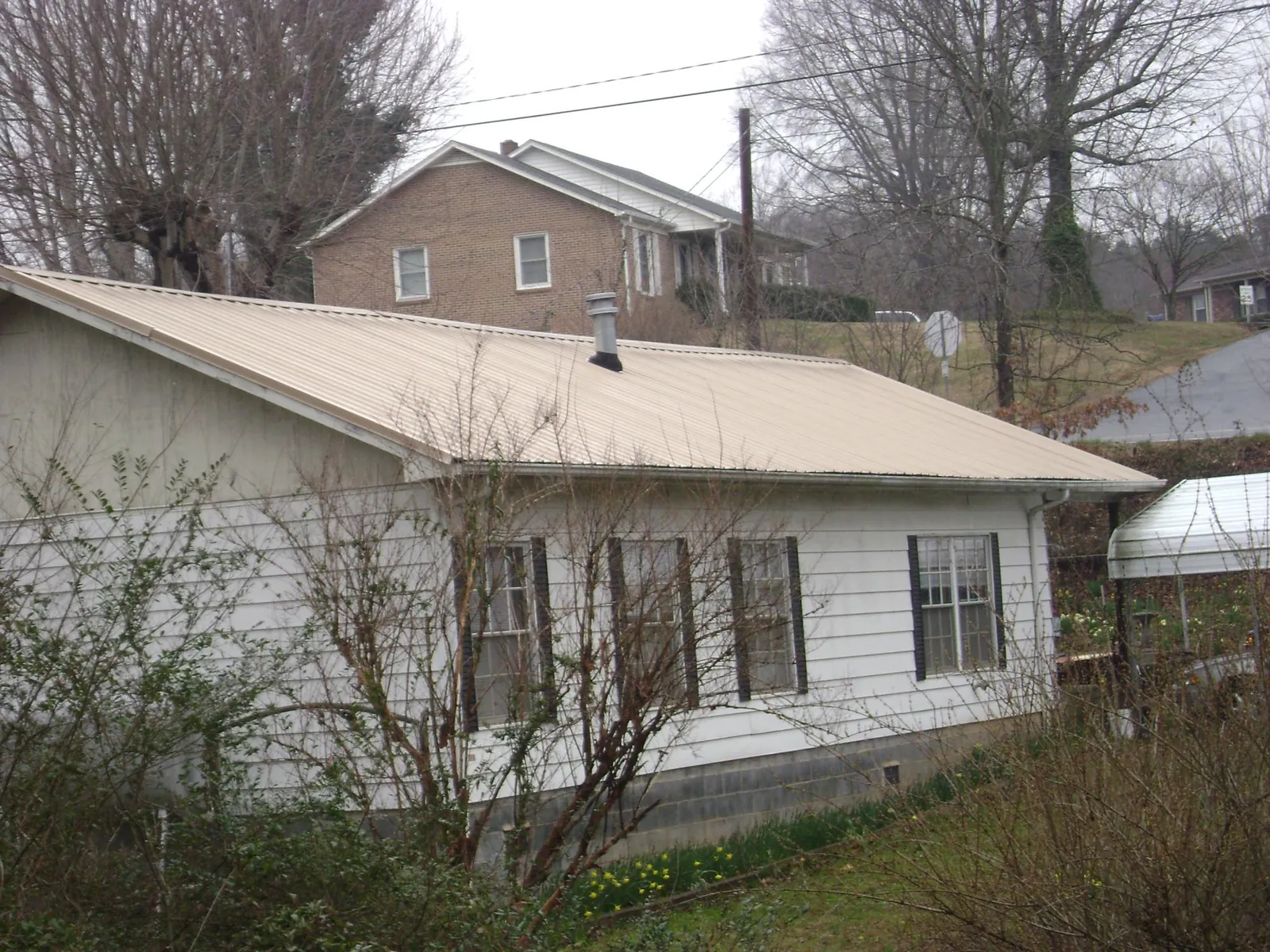Tan metal roof on a white sided house set into a hillside — Commercial Roofing by Roofing Brothers in Lucama