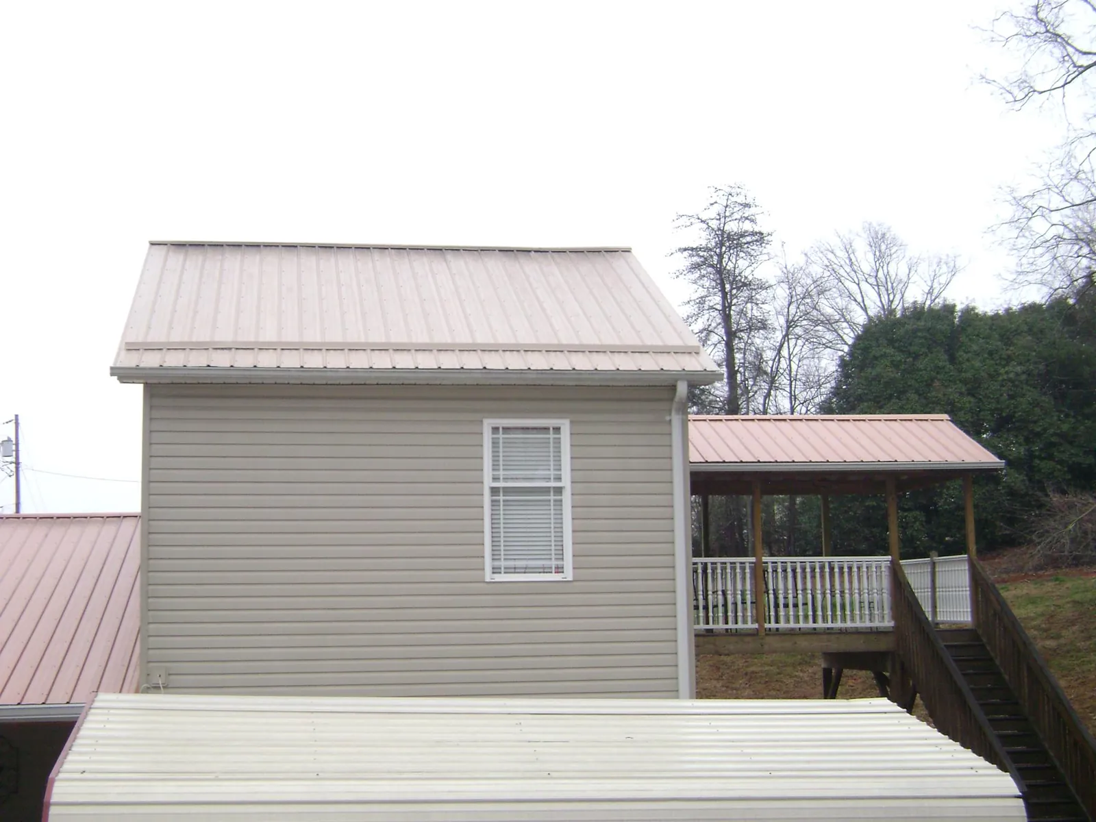 Tan metal roofs on a two story addition and attached porch, from a Roof Replacement job in Lucama